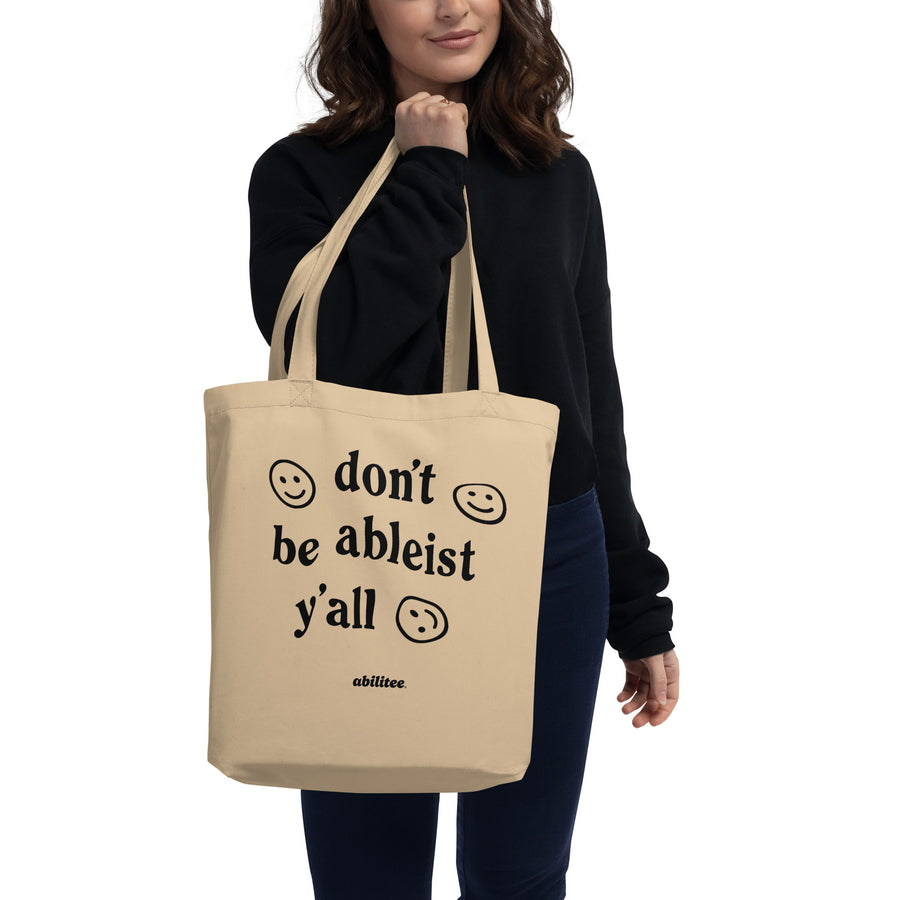 model holding natural color eco tote, with "don't be ableist y'all" printed in black on the front