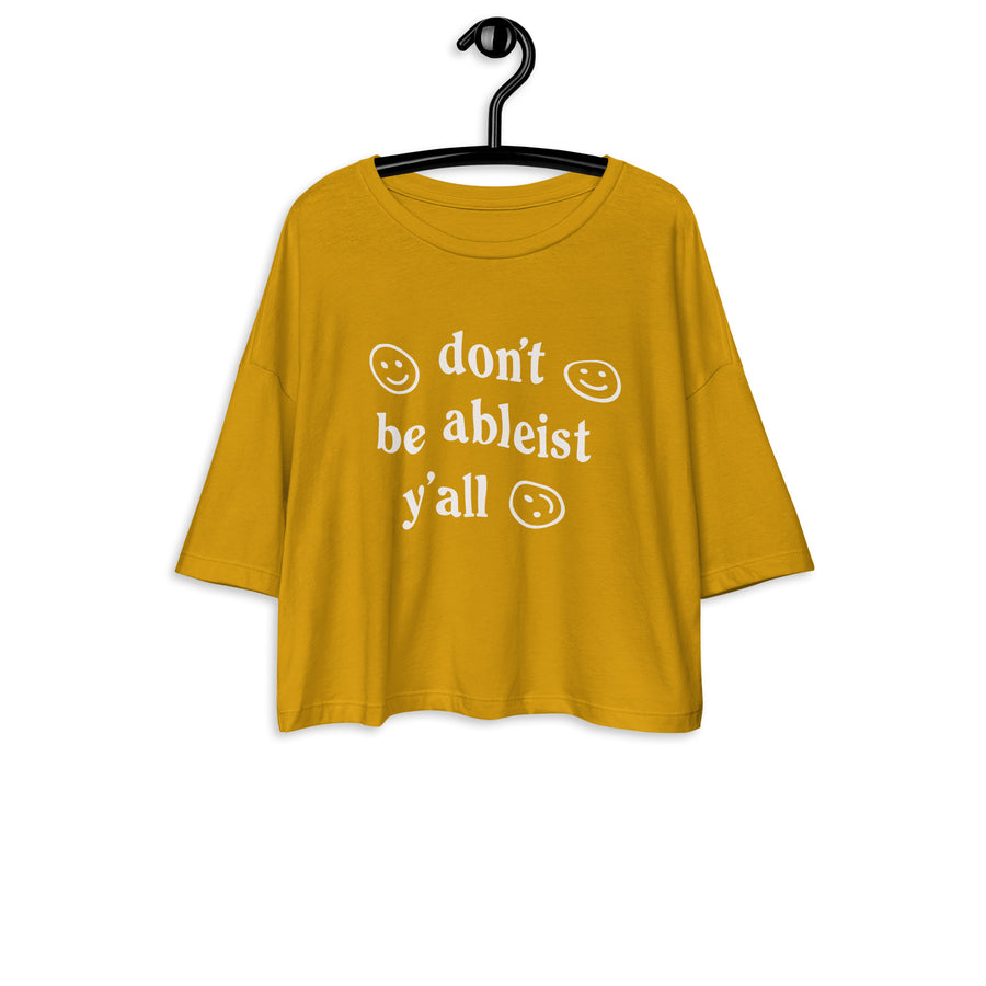 mustard yellow crop tee with drop shoulder, and "don't be ableist y'all" printed on the front in white with smiley faces, displayed on a hanger